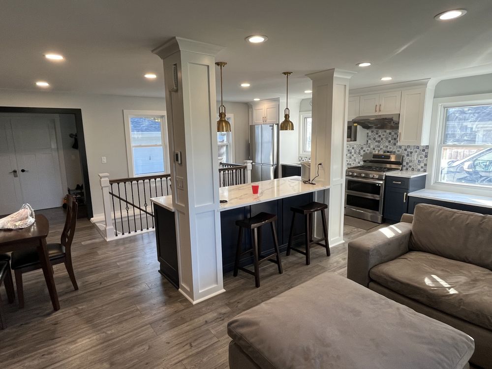 Modern open-concept kitchen and living area with light gray walls, wood flooring, a marble island, pendant lights, dark cabinets, and a cozy sofa.
