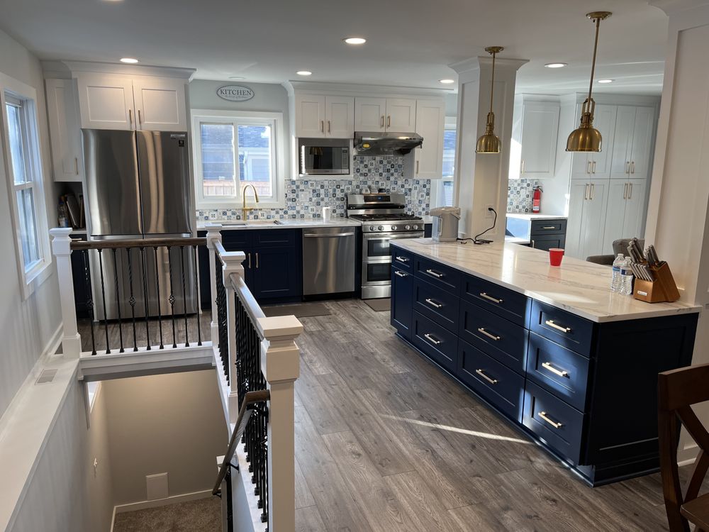 Spacious modern kitchen with navy and white cabinets, stainless steel appliances, and a large island. Elegant lighting and patterned backsplash.
